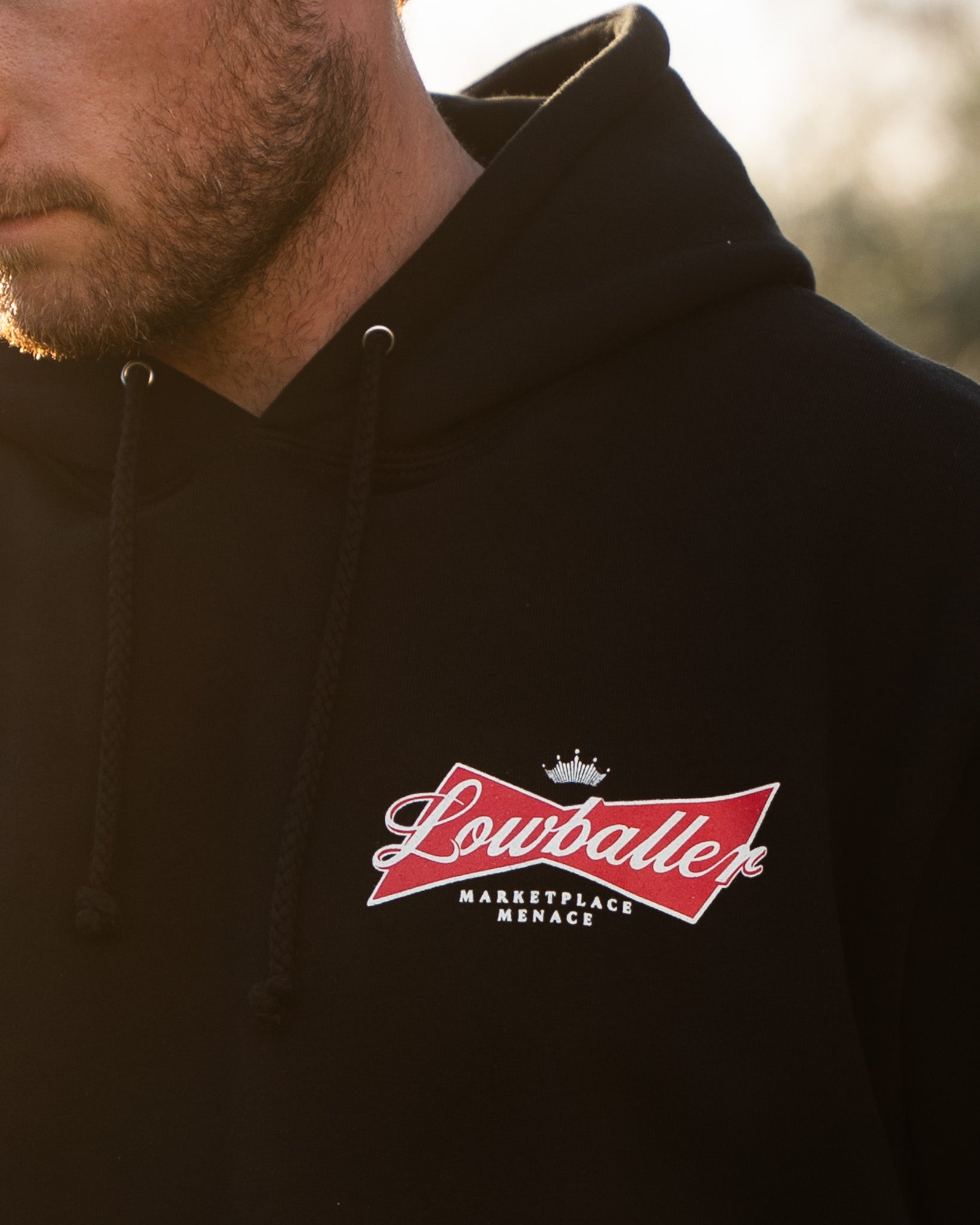 Black hoodie with a red and white logo on the chest against a blurred natural background