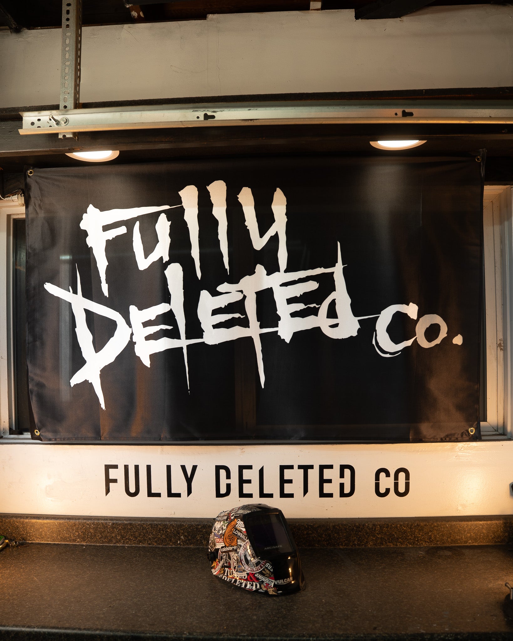 Black banner with 'Fully Deleted Co.' text on a vehicle, with a helmet on the ground.