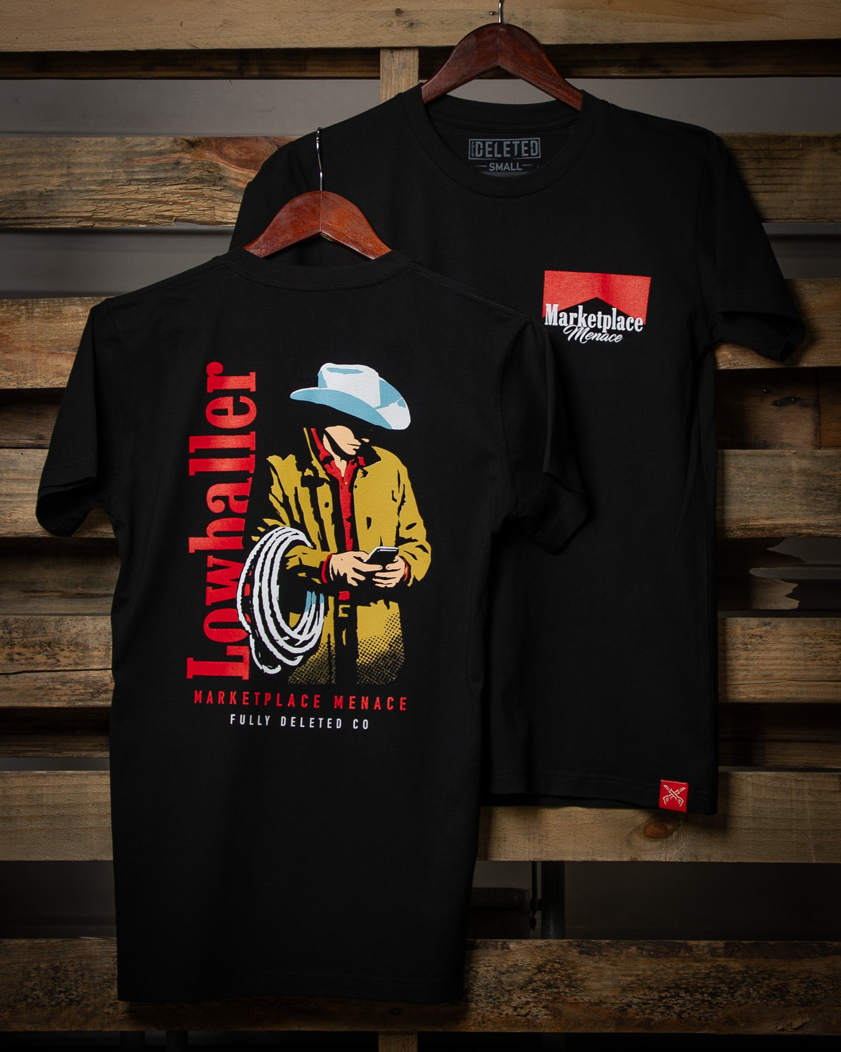 Black t-shirt with a graphic design of a person in a cowboy hat and jacket, held on a wooden hanger against a wooden background.